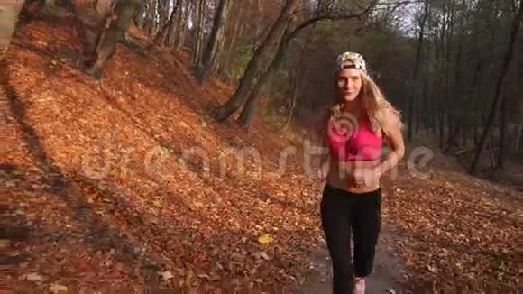 沿着秋天公园慢跑的迷人金发女人的特写镜头视频的预览图