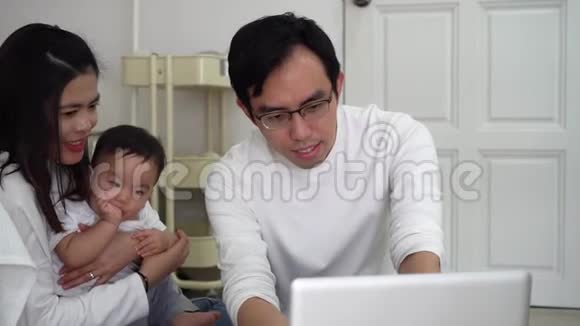 亚洲父亲和妻子一起用笔记本电脑工作还有一个可爱的亚洲小男孩坐在家里舒适的房间里视频的预览图