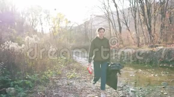 秋天风景中一个美丽的志愿者女孩在阳光下拿着塑料袋的肖像垃圾和塑料视频的预览图