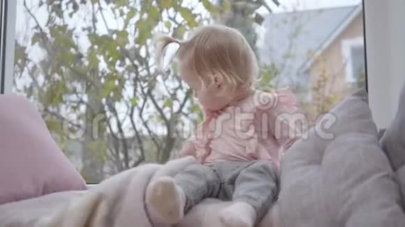 穿牛仔裤和粉红色衬衫的小可爱女孩在低窗台上软枕头上爬行的肖像白种人视频的预览图