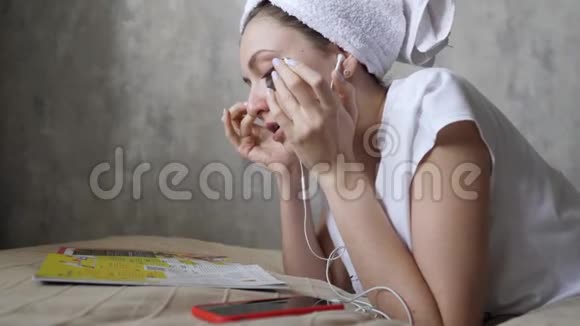 有魅力的女孩头上戴着毛巾贴着补丁看杂志听音乐环保保湿化妆品视频的预览图