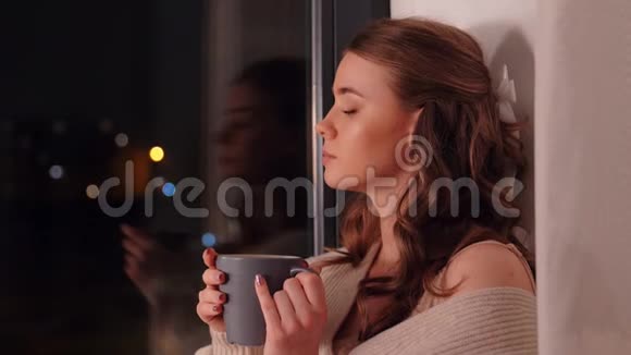 在窗口喝咖啡或茶的年轻女子视频的预览图