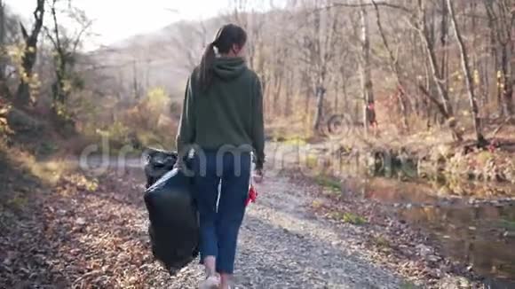 环境污染志愿服务理念一个年轻的女人手里拿着黑色塑料袋和手套走路视频的预览图
