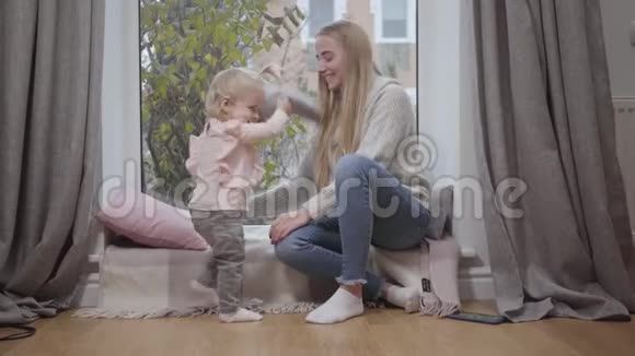 漂亮的白人女婴用柔软的枕头玩耍和年轻的母亲一起玩得很开心坐在那里的快乐女人视频的预览图