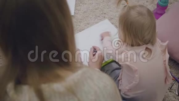 年轻的白种人女人和小女孩用彩色铅笔画画的俯视图妈妈在玩耍和教育她视频的预览图