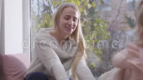 可爱的小白种人孩子带着白色柔软的泰迪熊给坐在低窗台上微笑的年轻女人快乐视频的预览图