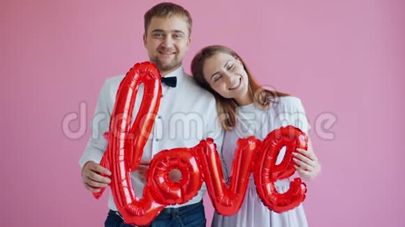 快乐的女孩和男孩站在粉红色的背景上拿着英语单词Love视频的预览图