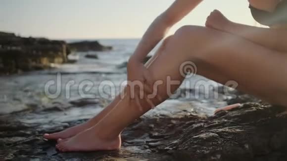 女人正在腿上擦防晒霜坐在海边视频的预览图
