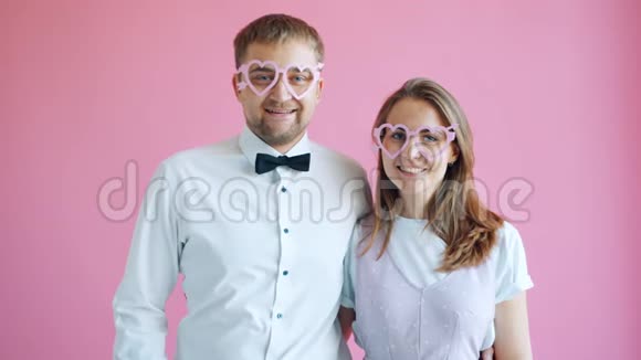 一对戴心形眼镜的男女在粉红色背景上微笑的肖像视频的预览图