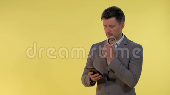 穿西装的年轻商人看着智能手机在黄色背景下思考一些事情视频的预览图