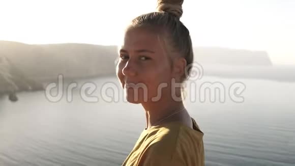 悬崖边上一个穿着黄色T恤的美丽金发旅行女孩的肖像欣赏着风景微笑着视频的预览图