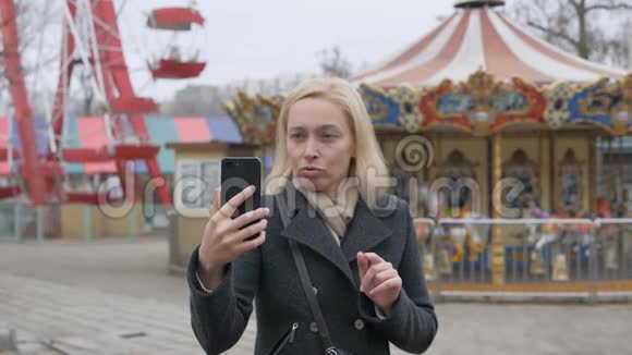 一个女人站在一个废弃的游乐园里在视频聊天效使智能手机摄像头源源不断视频的预览图