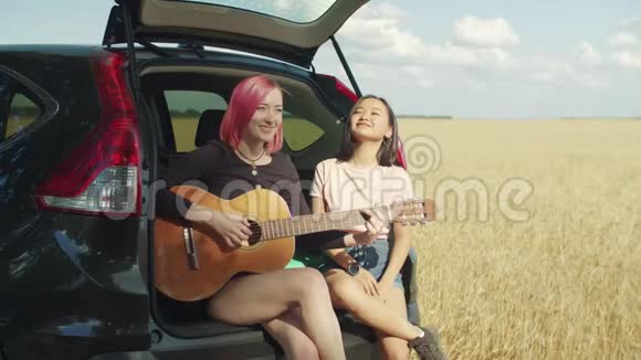 坐在汽车后备箱里弹吉他的时髦女人视频的预览图