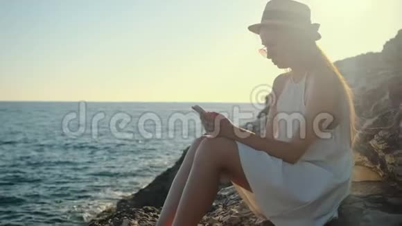 女人正在看一个坐在海边悬崖上的智能手机视频的预览图