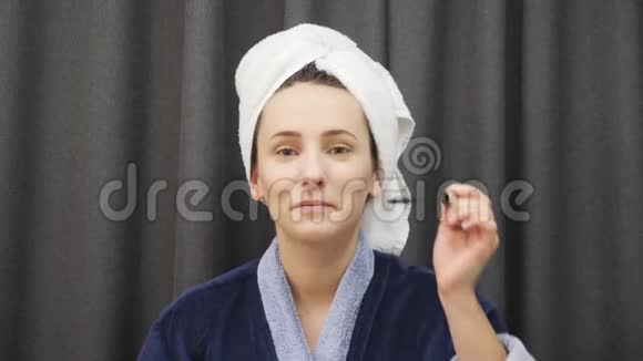 年轻女性在睫毛上涂睫毛膏女人穿着蓝色的浴袍头上拿着睫毛膏在家化妆妇女视频的预览图