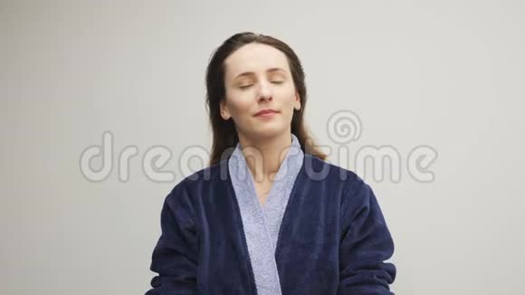 女人在白色背景下用梳子梳头发年轻自信的女性穿着蓝色浴袍在睡觉前梳头视频的预览图