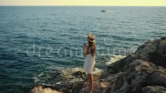 女人正在用智能手机在岩岸拍摄海水视频的预览图