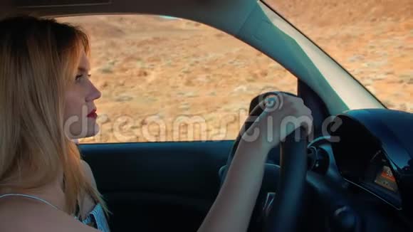 漂亮的金发女人开车握着方向盘窗外是一个火山形成的沙漠景观视频的预览图