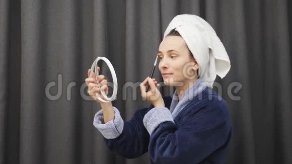 穿着浴袍化妆的女人美丽的年轻女性穿着蓝色浴袍和毛巾在灰色背景下涂上眼影Woma视频的预览图