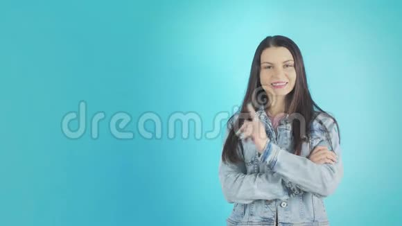 穿着牛仔夹克的微笑的年轻女子在蓝色的背景上竖起大拇指视频的预览图