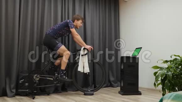 男子在固定式智能自行车教练机上完成自行车训练年轻的男自行车手关掉自行车电脑停了踏板视频的预览图