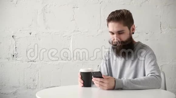 一个满脸胡子的快乐男人坐在办公桌前桌上有电话喝着咖啡视频的预览图