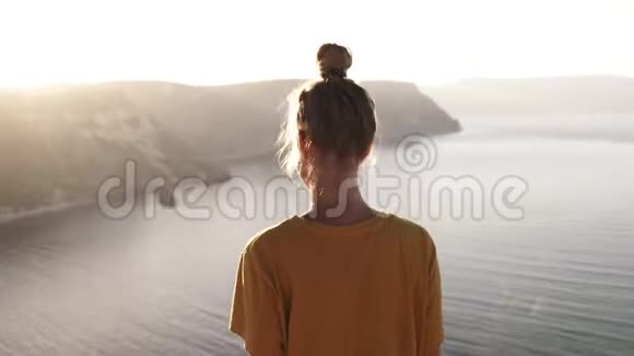 身着黄色T恤的女露营者的后侧场景展开双手迎接朝阳站在山上视频的预览图