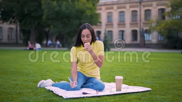 异国情调的学生女孩在午餐时间坐在公园里吃三明治女孩做作业视频的预览图