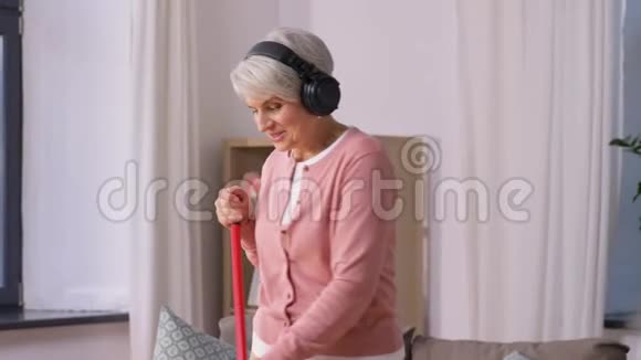 戴着耳机拿着扫帚打扫地板的老太太视频的预览图