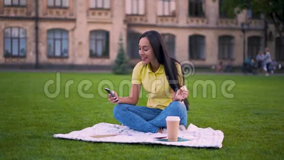 去野餐的快乐女孩女孩滚动手机笑吃三明治4K视频的预览图
