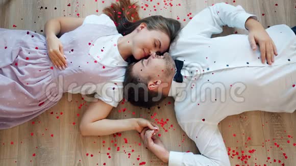 美丽的一对夫妇面对面地躺在地上而心形的纸屑却掉了下来视频的预览图