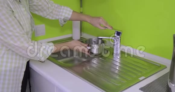 女人在浅绿色厨房的金属小锅里倒水视频的预览图