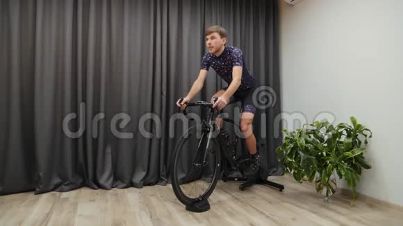 男性自行车运动员在室内训练自行车教练年轻的健身男子骑自行车在智能教练运动员骑自行车离开马鞍Cyc视频的预览图