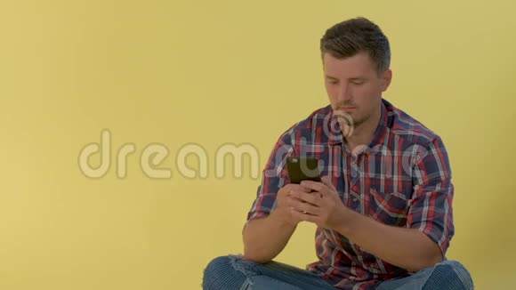 快乐的男人穿着格子衬衫坐在地板上在智能手机上聊天视频的预览图