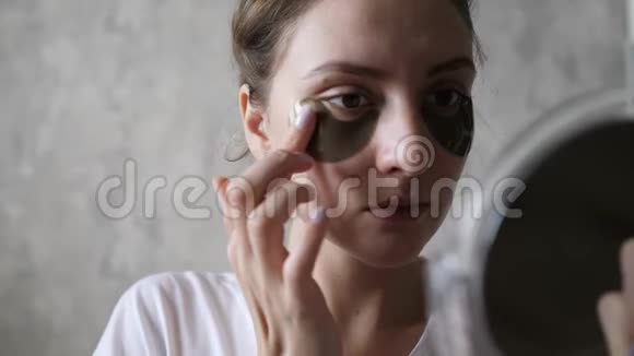 眼睛下面的皮肤提升一个健康的女孩在镜子里看自己使用天然化妆品视频的预览图