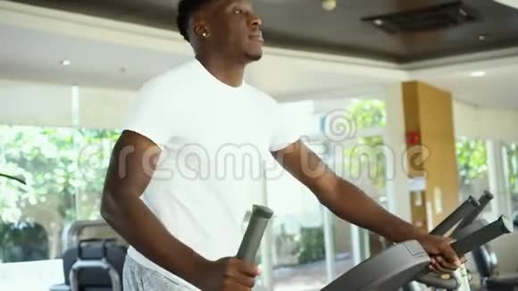 穿运动装的非裔美国人在现代健身房锻炼时在椭圆机上做台阶视频的预览图