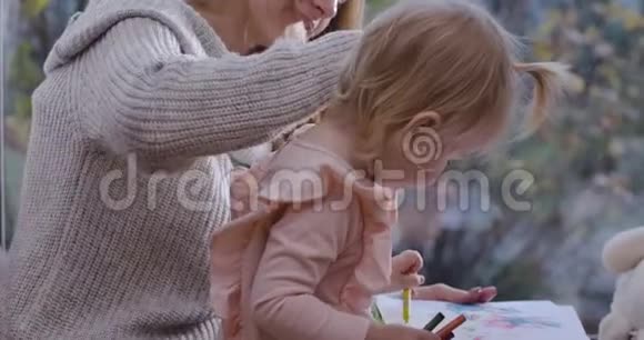 一个金发小孩子和她的母亲坐在低矮的窗台上用铅笔画画年轻的微笑女人视频的预览图