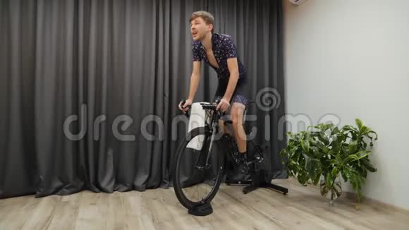 人骑着智能家居室内循环教练车从马鞍上出来喝等渗或水穿着专业的自行车服装在视频的预览图