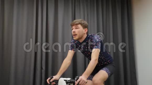 男子训练自行车智能教练减肥将男性自行车骑在自行车上喝等渗酒在室内拿毛巾在视频的预览图