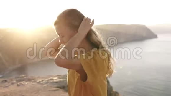 美丽的金发女孩穿着黄色的T恤梳着她的头发站在前面如果群山的喧闹景象太阳视频的预览图