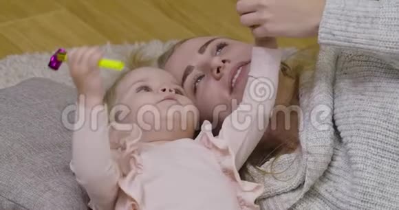 近距离观看美丽的高加索女人和小可爱女孩躺在蓬松的地毯上快乐母亲的肖像视频的预览图