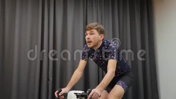 骑在家用智能自行车教练车上的人的肖像室内训练概念年轻的高加索运动员在自行车上艰苦训练视频的预览图