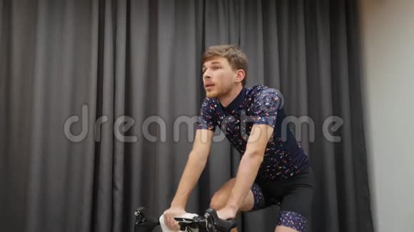 年轻自信的男子骑自行车在室内智能教练画像健身男性在家骑自行车艰苦训练骑自行车应用程序视频的预览图