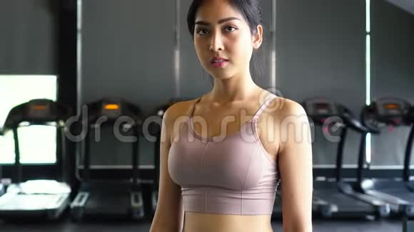 微笑和坚定的年轻亚洲女运动员一边看镜头一边交叉双臂站在健身房视频的预览图