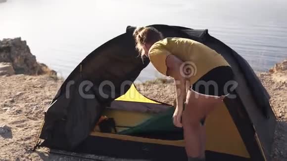 一个穿黄色T恤的女人在露营帐篷里搭床垫从悬崖顶端拍摄的画面露营视频的预览图