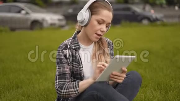 中弹在平板电脑上看有趣视频的女孩使用大耳机播放音乐并在平板电脑上滚动新闻视频的预览图