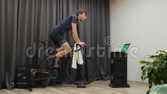 专业的男性骑自行车者从马鞍上骑下来在固定的智能自行车教练机上踩着沉重的齿轮减肥康塞普视频的预览图