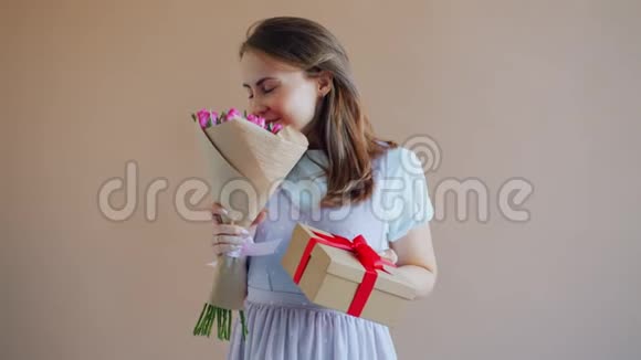 快乐女孩拿着米黄色背景的礼品盒闻花香的慢动作视频的预览图