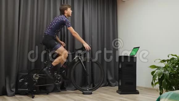 男性在家庭自行车智能教练上做自行车训练穿自行车服装的自信男人在家骑自行车锻炼出汗视频的预览图