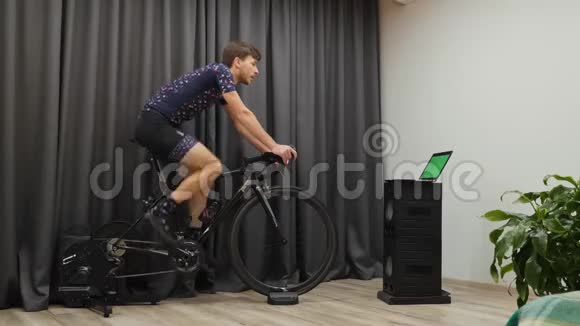 年轻的运动男性喝精力充沛的饮料而骑自行车的家庭智能自行车教练有动力的三项运动员准备三项比赛视频的预览图